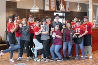 A group of CC’s team members smile and pose together inside the cafe, holding drinks.